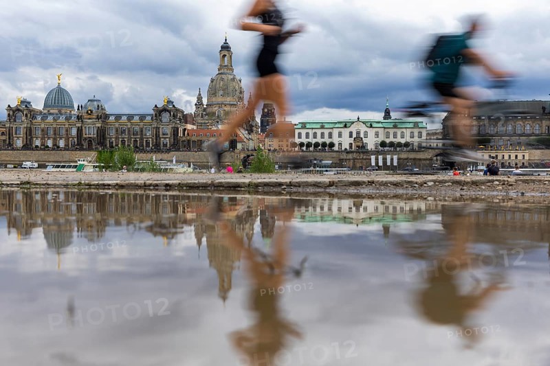 The silhouette of Dresden with a cyclist and a jogger and dark clouds behind the Church of Our Lady is reflected in a puddle on the Elbe cycle path, Elbe cycle path, Dresden, Saxony, Germany, Europe