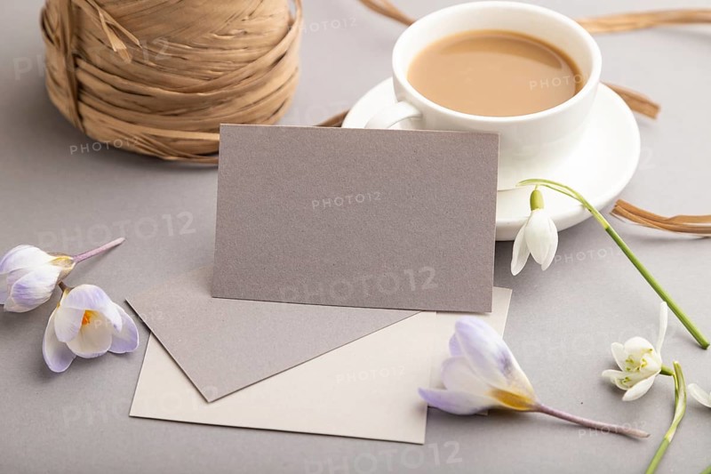Gray paper business card mockup with spring snowdrop crocus and galanthus flowers and cup of coffee on gray background. Blank, business card, side view, copy space, still life. spring concept