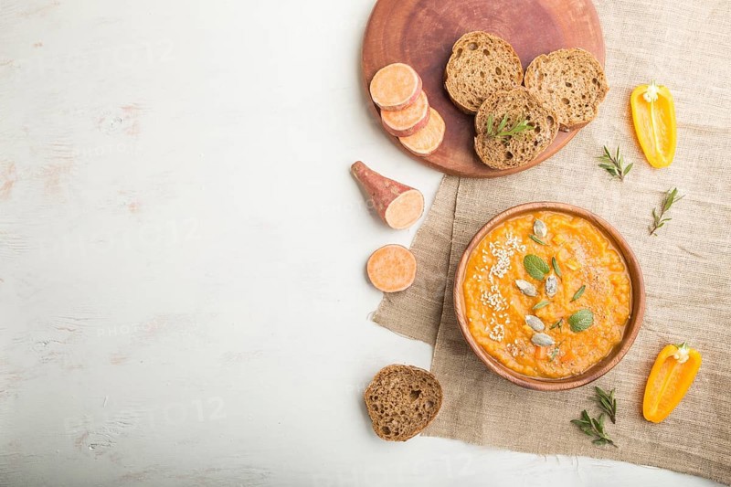 Sweet potato or batata cream soup with sesame seeds in a wooden bowl on a white wooden background with linen textile. top view, flat lay, copy space