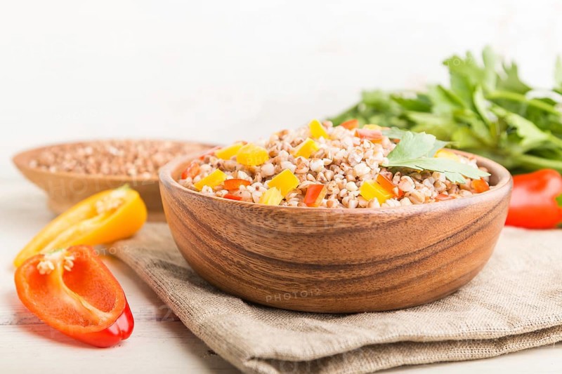 Buckwheat porridge with vegetables in wooden bowl on a white wooden background and linen textile. Side view, copy space, selective focus. Russian traditional cuisine