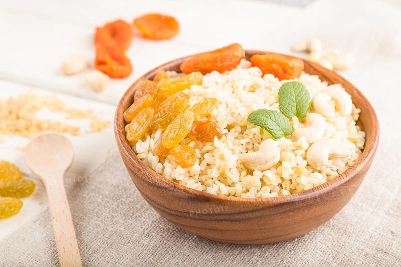 Bulgur porridge with dried apricots, raisins and cashew in wooden bowl on a white wooden background and linen textile. Side view, close up, selective focus. Turkish traditional cuisine