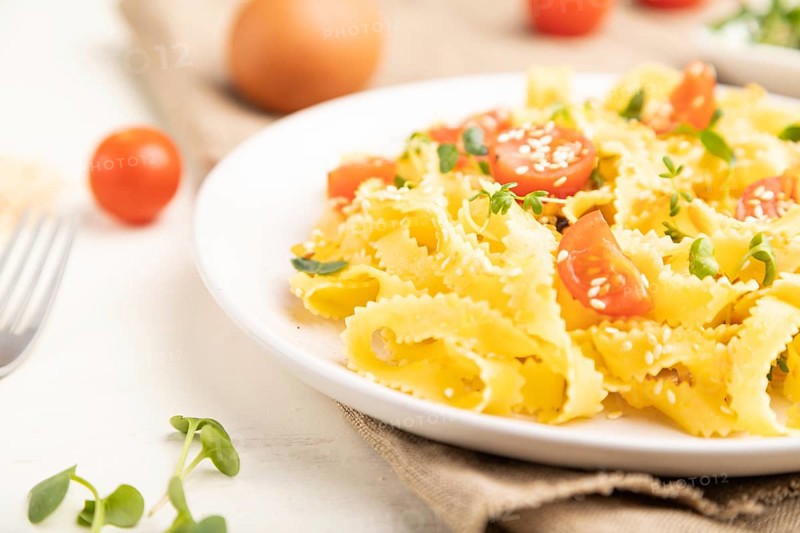 Reginelle semolina pasta with tomato, eggs, sesame and microgreen sprouts on a white wooden background and linen textile. Side view, close up, selective focus