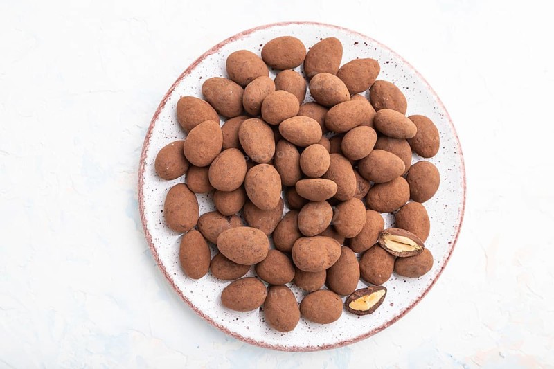 Almond in chocolate dragees on ceramic plate on white concrete background. Top view, close up, flat lay