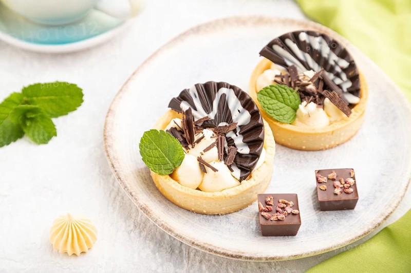 Sweet tartlets with chocolate and cheese cream with cup of coffee on a gray concrete background and green textile. Side view, close up, selective focus