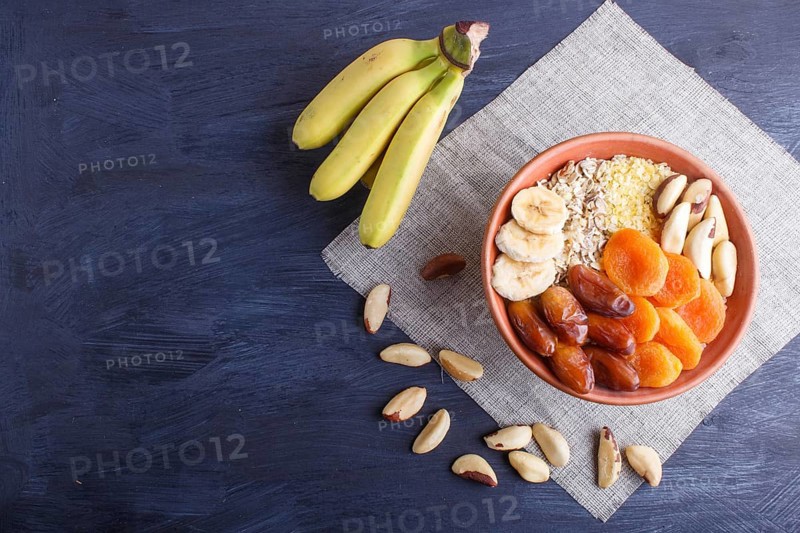 A plate with muesli, banana, dried apricots, dates, Brazil nuts on a black wooden background. top view. copy space