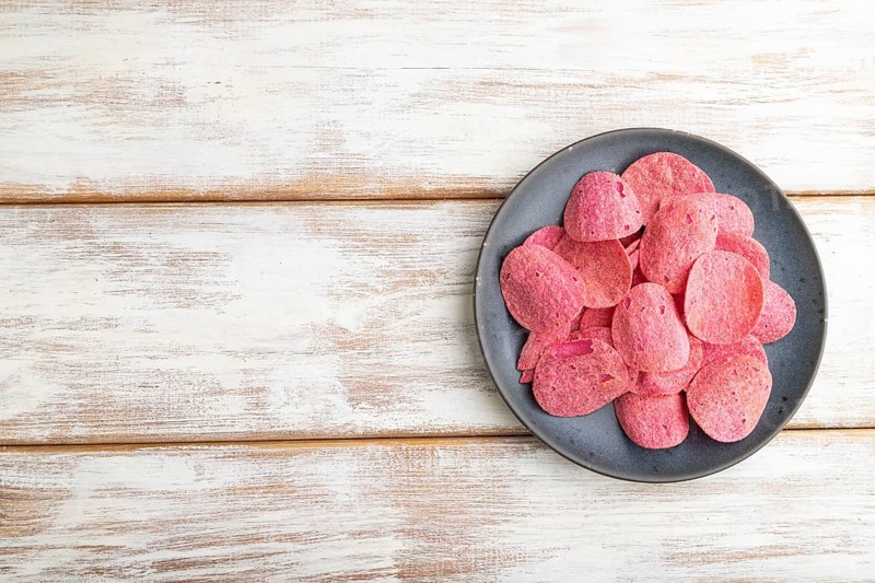 Red potato chips with herbs and tomatoes on white wooden background. Top view, flat lay, copy space