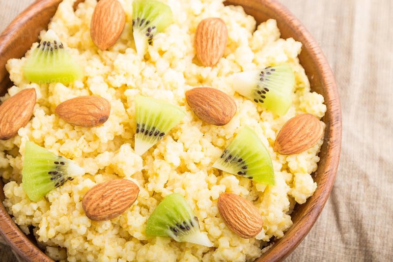 Millet porridge with kiwi and almonds in wooden bowl on a white wooden background and linen textile. Top view, close up, selective focus