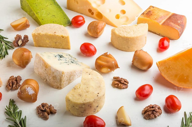 Set of different types of cheese with rosemary and tomatoes on a white wooden background. Side view, close up
