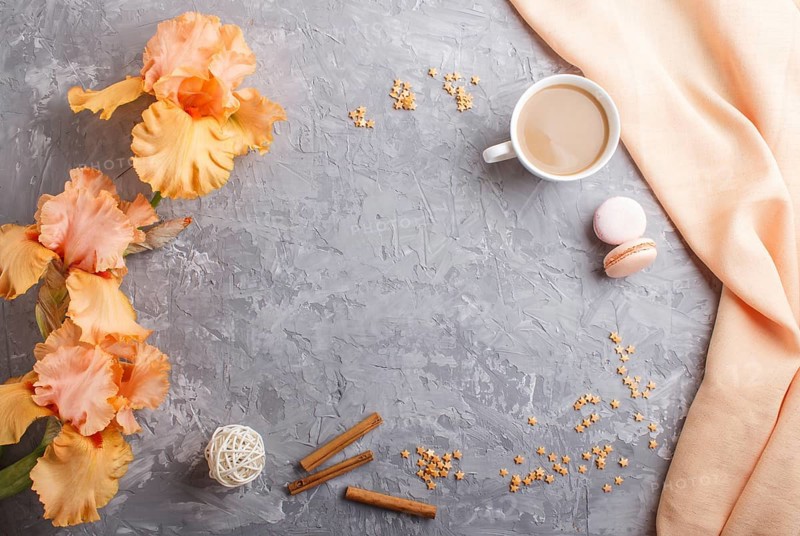 Orange iris flowers and a cup of coffee on a gray concrete background. Morninig, spring, fashion composition. Flat lay, top view, copy space