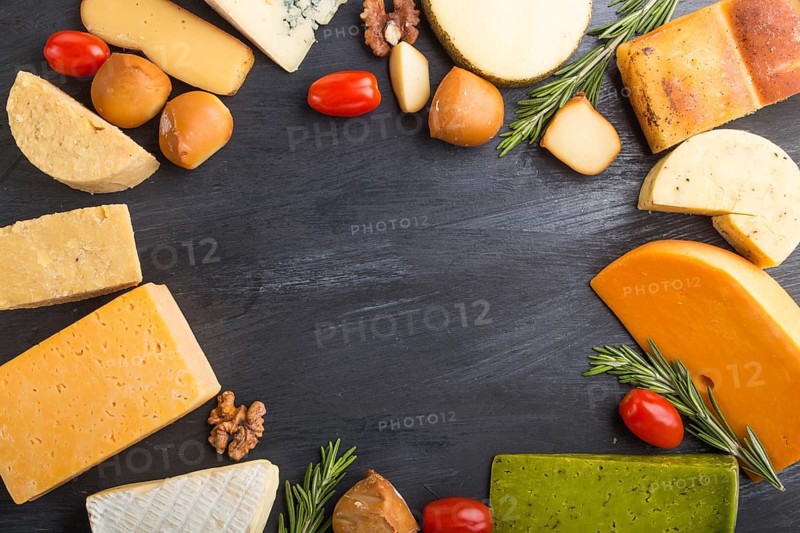 Set of different types of cheese with rosemary and tomatoes in the shape of a frame on a black wooden background. Top view, flat lay, copy space