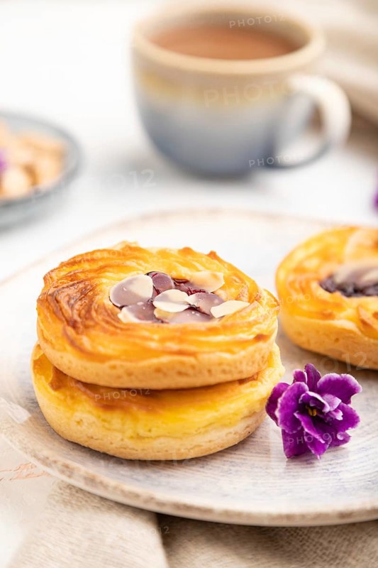 Small cheesecakes with jam and almonds with cup of coffee on a white concrete background and linen textile. Side view, close up, selective focus