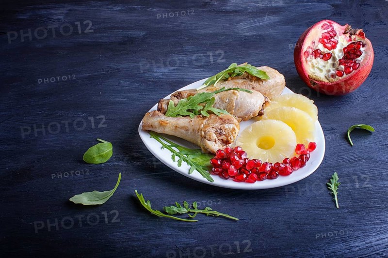 Fried chicken legs with rucola, pineapple and pomegranate seeds on black wooden background, copy space, close up