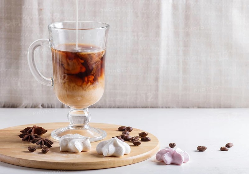 Glass cup of coffee with cream poured over and meringues on a wooden board on a white background. close up, copy space