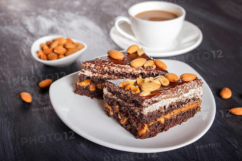 Chocolate cake with caramel, peanuts and almonds on a black wooden background. cup of coffee, close up