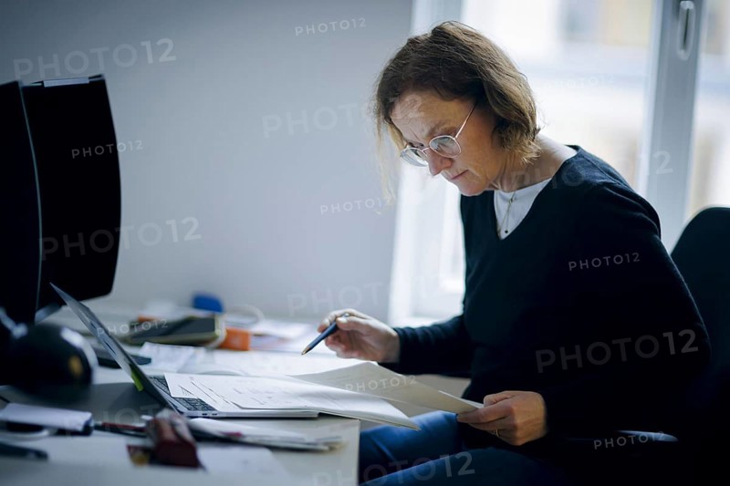 Symbolic photo on the subject of analogue organisation of papers. A woman sits at her desk in the office and works with documents. Berlin, 16.01.2024