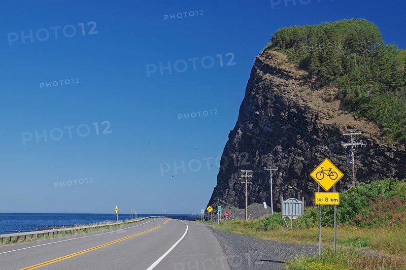 A road along a large cliff with a view of the sea and road signs indicating a cycle path, Gaspesie, St. Lawrence Srom, Quebec, Canada, North America