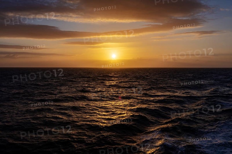 Sunset over a calm sea with clouds and a shimmering orange sky, Celtic Sea