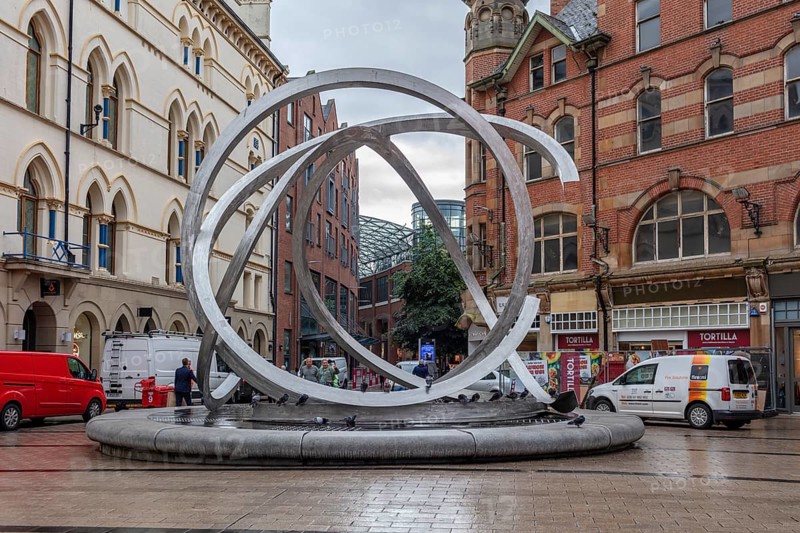Modern sculpture in a busy street scene with people and buildings, Belfast