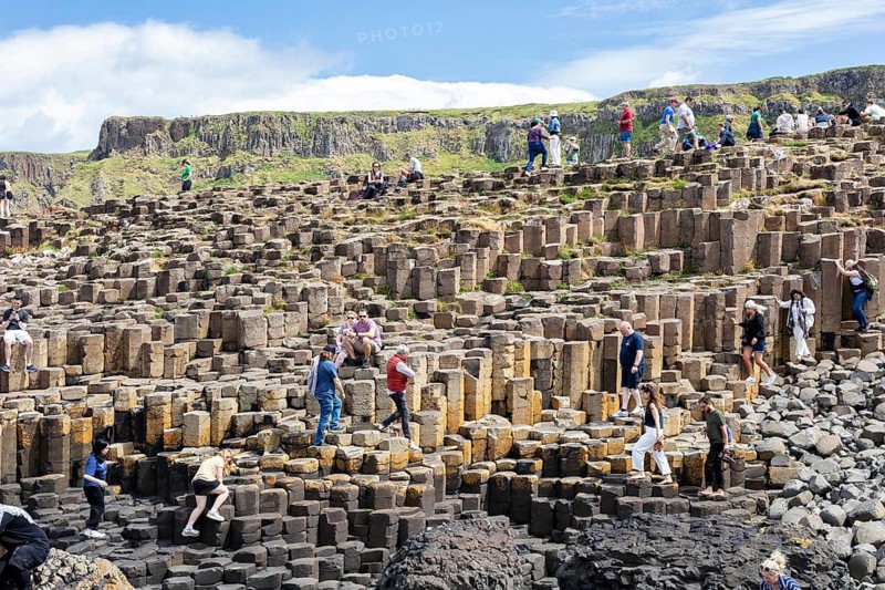 Tourists hike on staircase-shaped rock formations under a blue sky, Giant Causeway