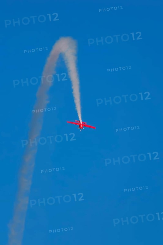 Red stunt aerobatic plane inverted flying loop performing stunts in blue sky. Concept of speed, difficulty, precision, risk