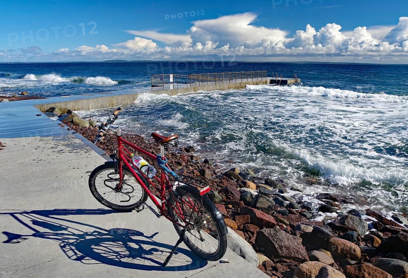 A red bicycle stands on the shore with a view of the rough sea and thick clouds in the blue sky, Tönsberg, Oslofjord, Norway, Europe