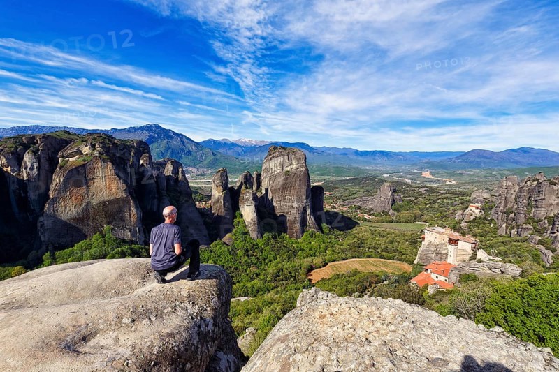 Tourist enjoys view of hermitages between high rocks, monasteries on sandstone formations, Meteora, blue sky, spring weather, Thessaly, Greece, Europe