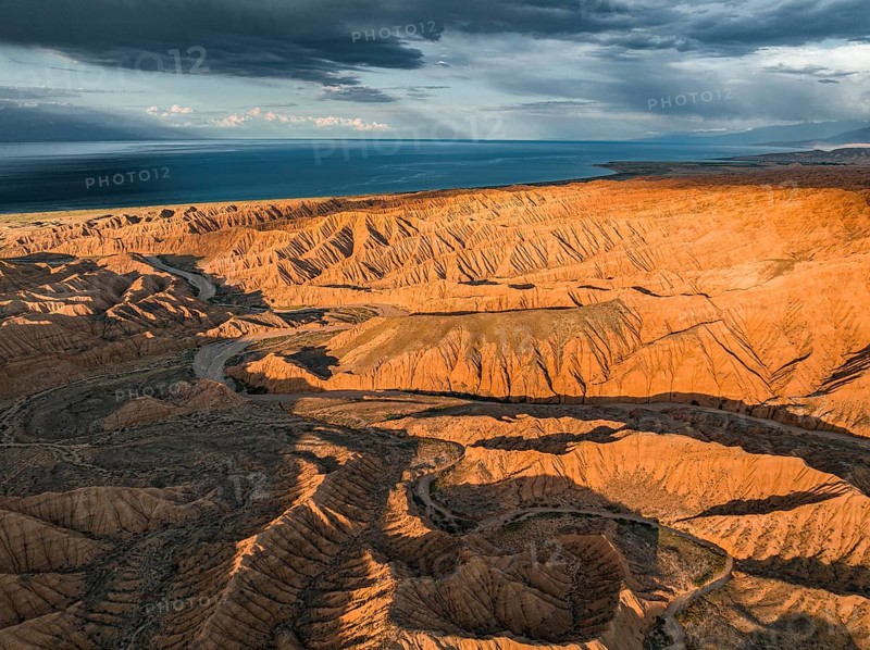 Riverbed runs through a landscape of eroded hills, badlands at sunset, Issyk Kul Lake in the background, aerial view, Canyon of the Forgotten Rivers, Issyk Kul, Kyrgyzstan, Asia