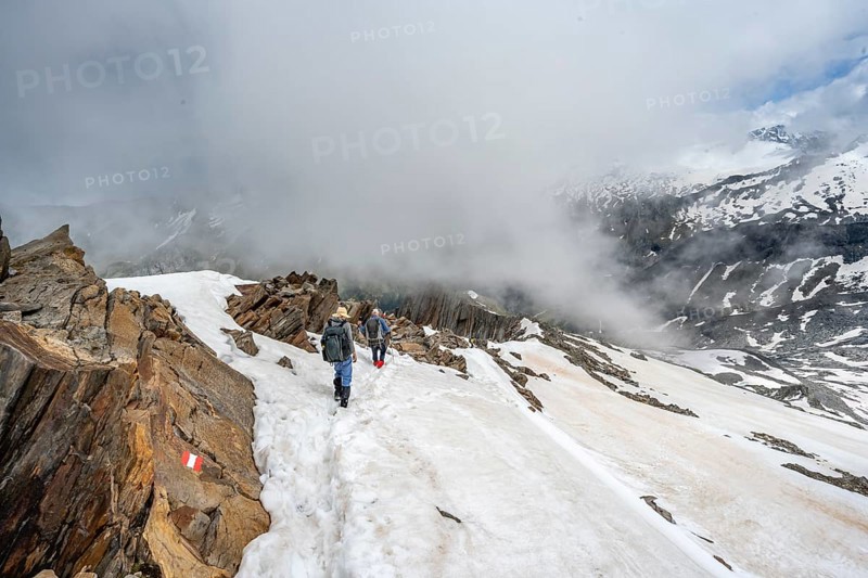 Mountaineer on a rocky ridge with snow, descent from the summit of Schönbichler Horn, view of snow-covered mountain peaks and valley Zemmgrund, Berliner Höhenweg, Zillertal Alps, Tyrol, Austria, Europe