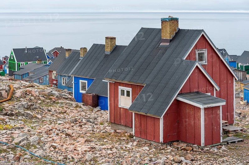 Colourful houses with black roofs stand on rocky ground near a grey coastline, fjord, remote Arctic Inuit settlement Ittoqqortoormiit, Scoresbysund or Scoresby Sund or Greenlandic Kangertittivaq, East Greenland, Greenland, North America