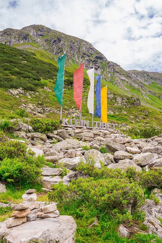 Scene in the mountains with colourful flags, a sign and green vegetation, surrounded by rocks, Klein Tibet, Zillertal, Austria, Europe
