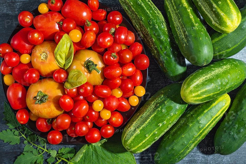 Fresh tomatoes (Solanum lycopersicum) and cucumbers (Cucumis sativus) with green leaves arranged on a surface
