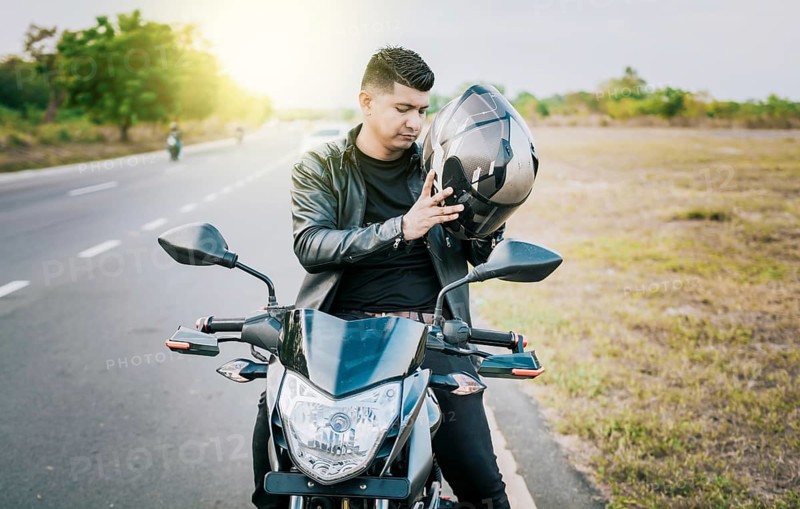 Young motorcyclist man putting on safety helmet outdoors. Male biker on motorcycle putting on helmet. Biker motorcycle safety concept