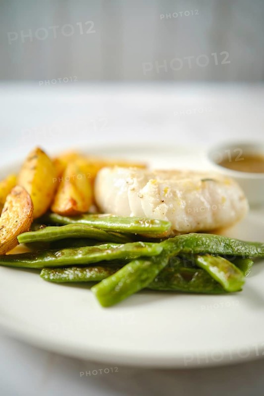 A tender fish fillet alongside fresh green beans and golden roasted potatoes. A small bowl of sauce complements the meal, creating an appetizing presentation