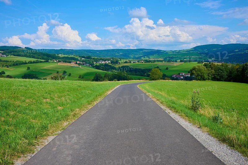 Asphalted road through green fields and rolling hills under a blue, cloudy sky, Wachtküppel, summer, Gersfeld, Rhön, Hesse, Germany, Europe