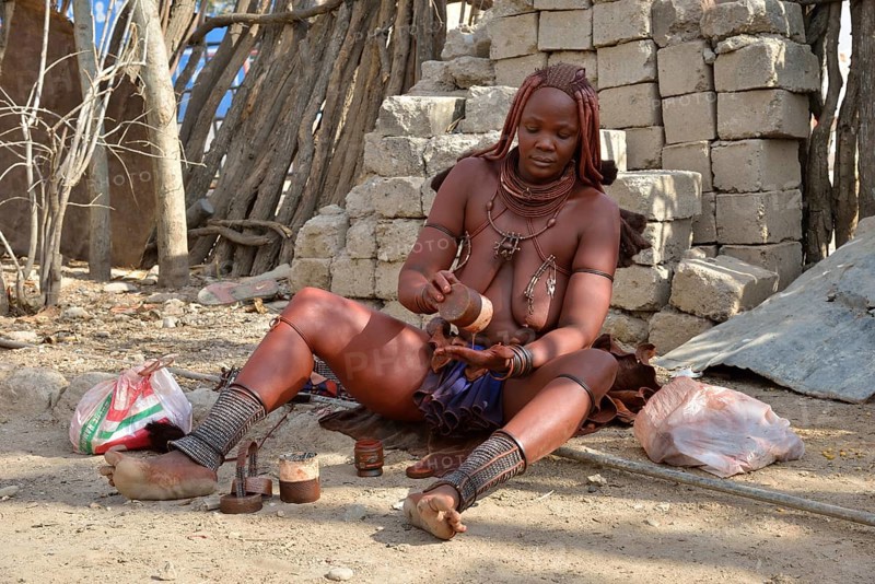 Himba woman applying perfume with traditional essences made of ground red iron rocks, butterfat and herbs of the Omuzumba shrub, Opuwo, Kaokoland, Kunene, Namibia, Africa