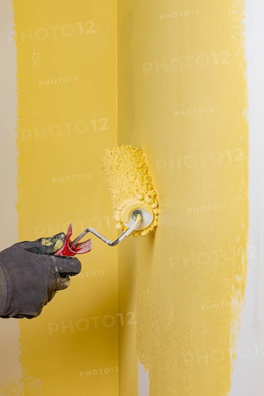 Wall is painted with yellow paint, hand with paint roller
