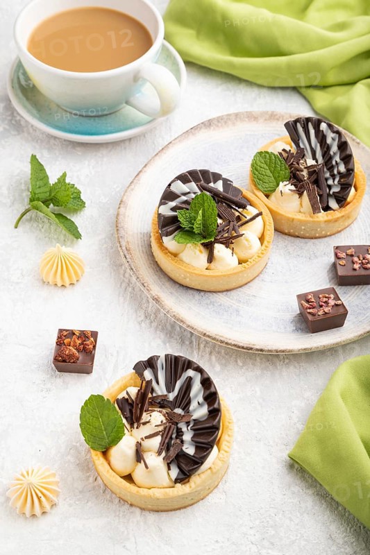 Sweet tartlets with chocolate and cheese cream with cup of coffee on a gray concrete background and green textile. Side view, close up