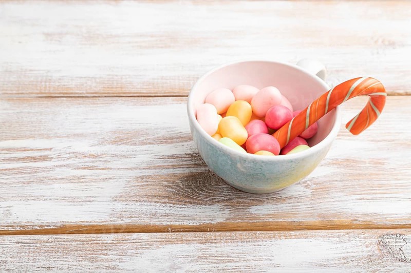 Heap of multicolored caramel candies in cup on white wooden background. copy space, side view, close up