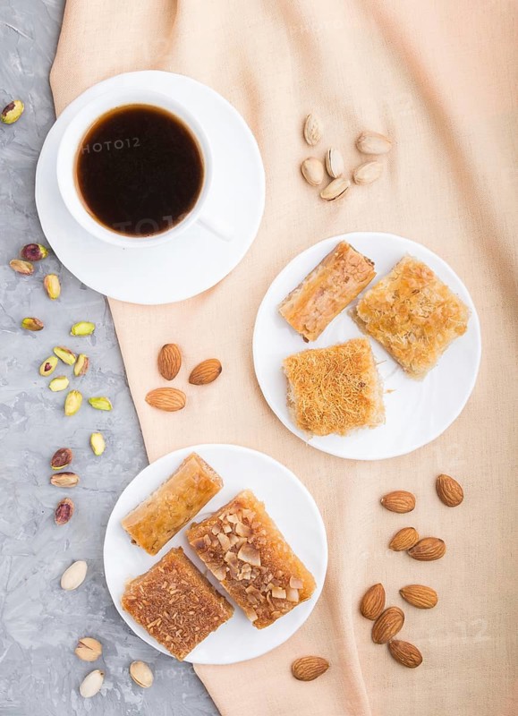 Traditional arabic sweets (basbus, kunafa, baklava) and a cup of coffee on a gray concrete background and orange textile. top view, flat lay, close up