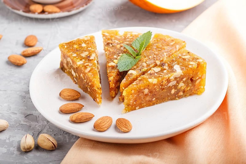 Traditional turkish candy cezerye made from caramelised melon, roasted walnuts, hazelnuts, cashew, pistachios on white ceramic plate and a cup of coffee on a gray concrete background. side view, close up, selective focus