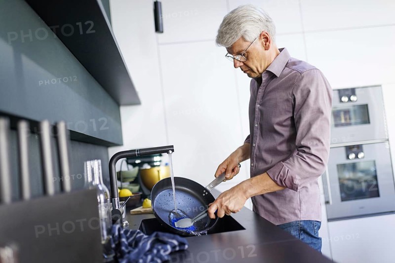 Symbolic photo. A man stands in the kitchen washing dishes. Berlin, 13.08.2024