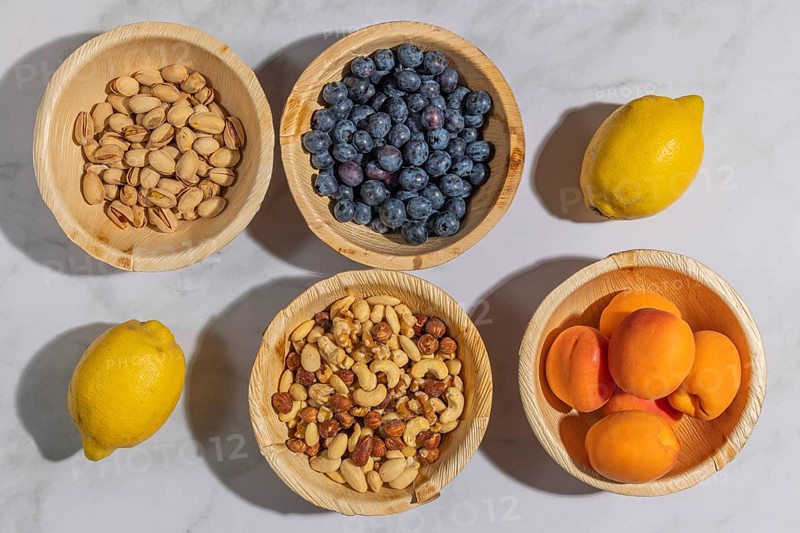Healthy food, lemons, nuts, blueberries, apricots and pistachios in wooden bowls, on a marble surface