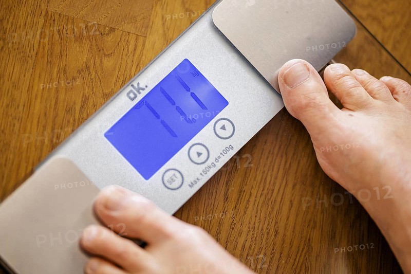 Symbolic photo on the subject of body weight. The feet of a 60-year-old person can be seen next to the weight display of a scale. Berlin, 13.08.2024