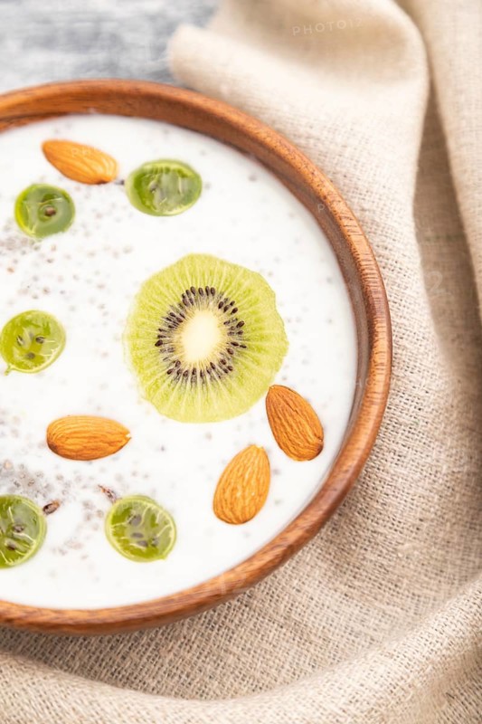 Yogurt with kiwi, gooseberry, chia and almonds in wooden bowl on gray wooden background and linen textile. Top view, close up, selective focus