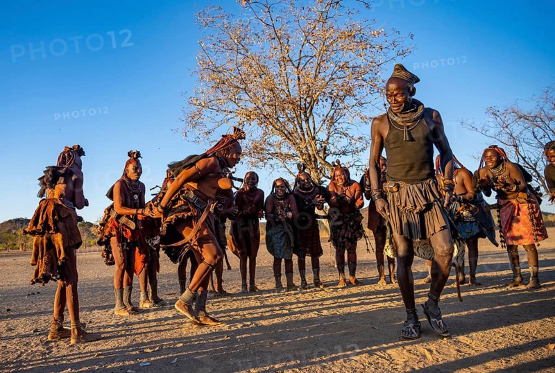 Group of traditional Himba woman with chief of the village standing in a semicircle, clapping and dancing, music and dance, in the evening light, near Opuwo, Kaokoveld, Kunene, Namibia, Africa