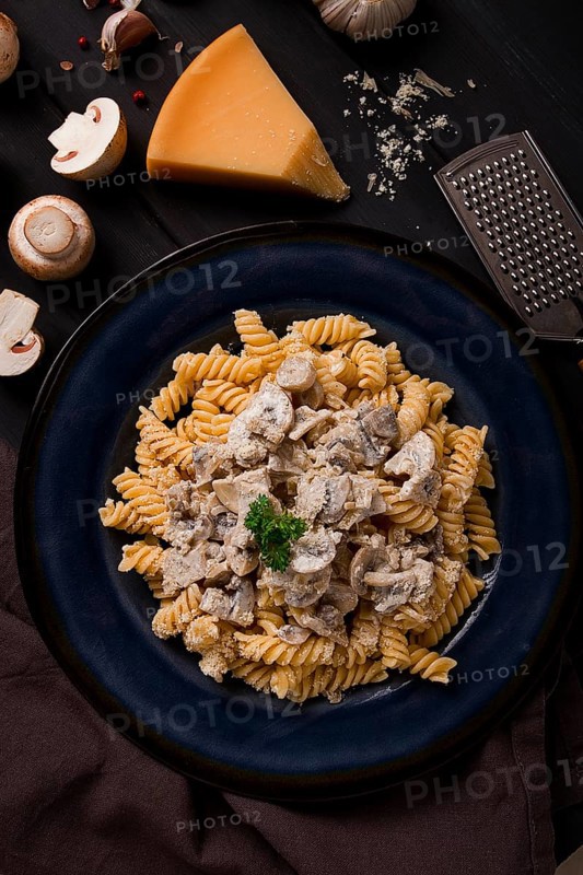 Fusilli pasta, with champignons in cream sauce, top view, with ingredients, on a wooden table, no people