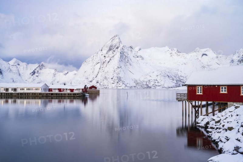 Rorbuer huts of Hamnoy at the fjord, snowy mountains in the background, Hamnøy, Reine, Moskenesøya, Lofoten, Norway, Europe