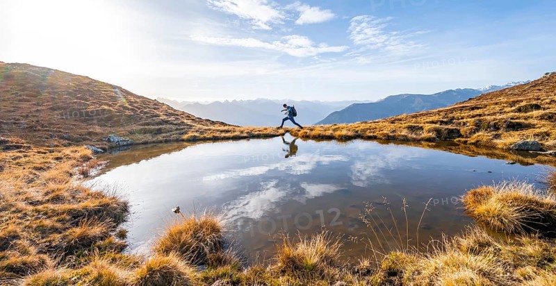 Mountaineer jumping, reflected in a small mountain lake on the Krahberg, mountain panorama in autumn, Venet crossing, Ötztal Alps, Tyrol, Austria, Europe