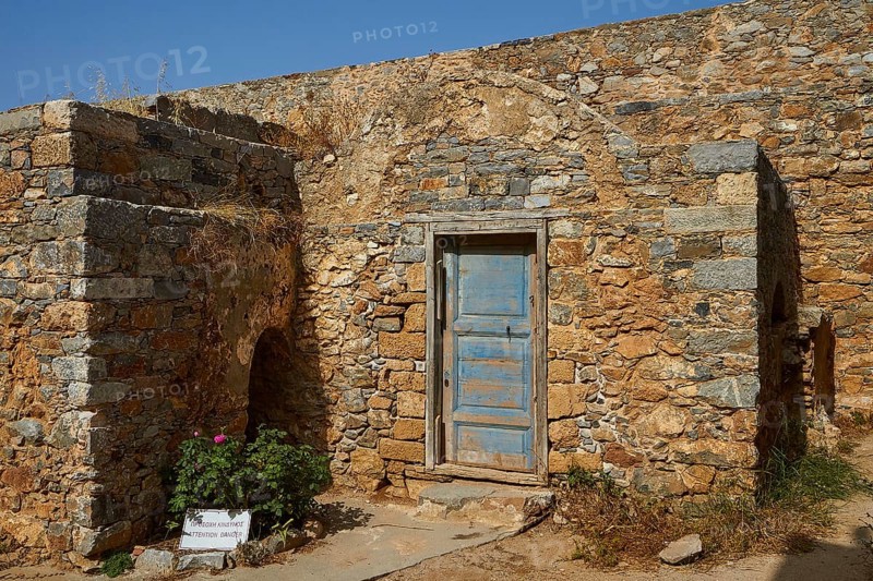 Old stone house with a blue door surrounded by historical ruins and a flowering bush, Venetian Sea Fortress, Leper Island, Spinalonga, Elounda Bay, Mirabello Bay, East Crete, Crete, Greek Islands, Greece, Europe