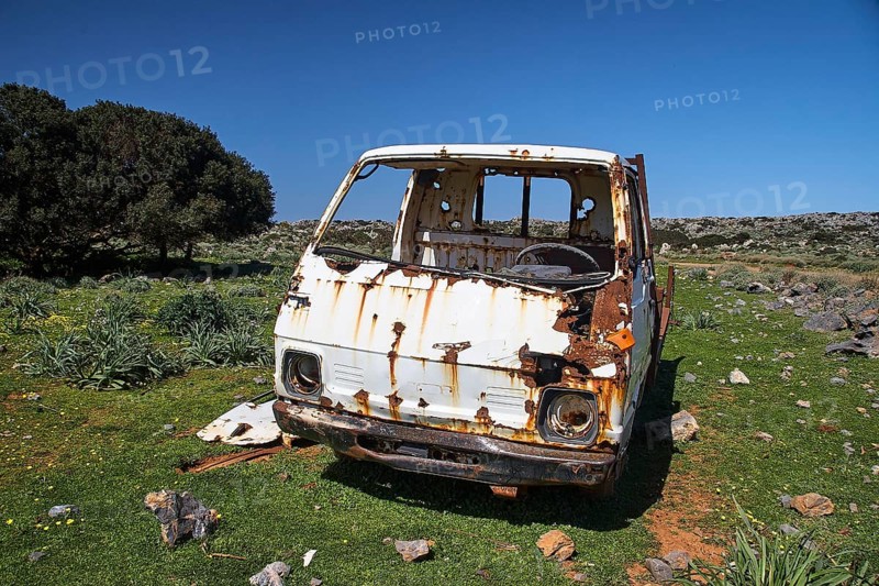 A rusty, abandoned van stands in a meadow with green grass and trees under a blue sky, wrecked vehicle, Crete, Greek Islands, Greece, Europe